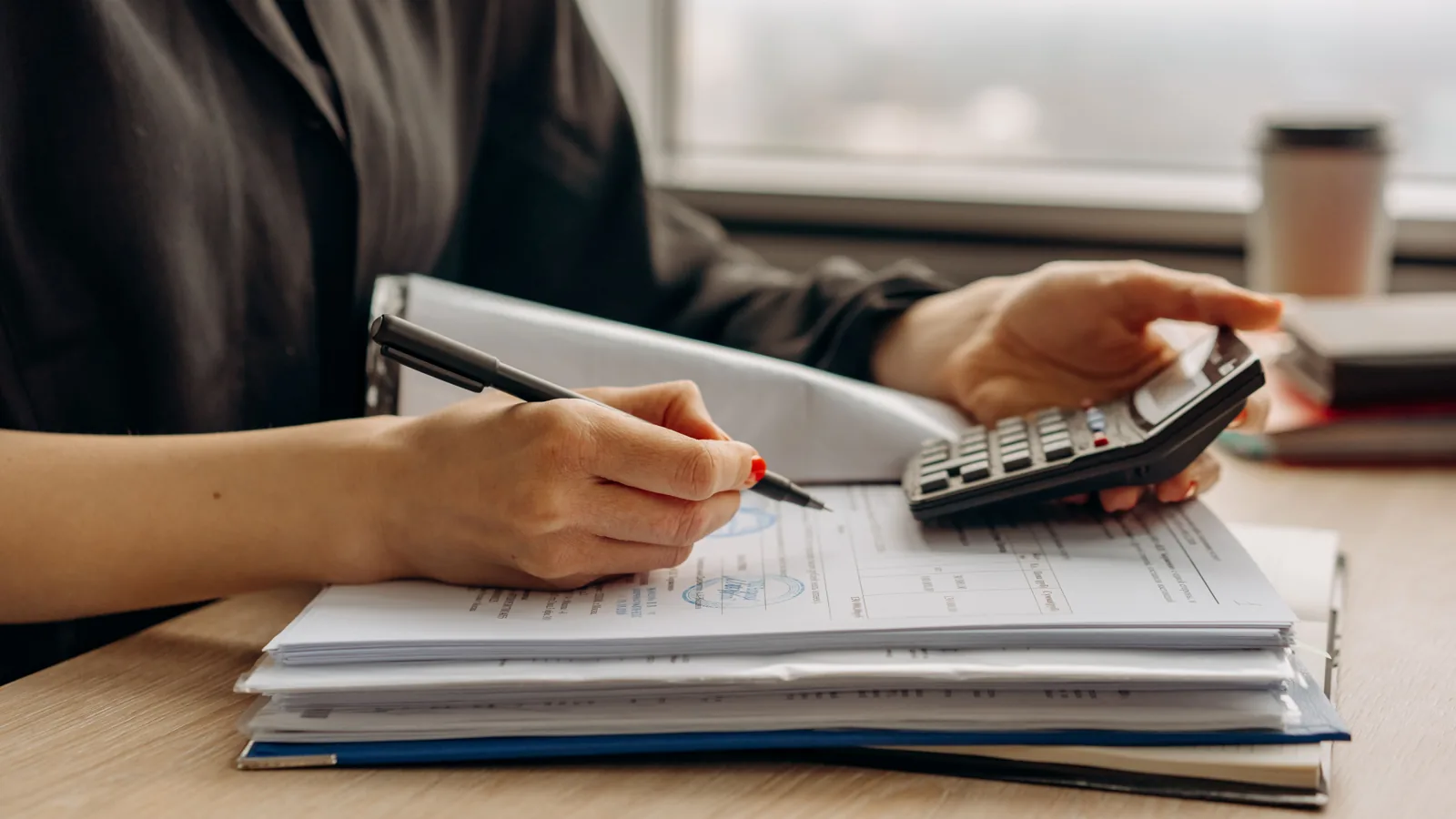 Mains qui pointent des chiffres sur une pile de documents avec un stylo et une calculatrice