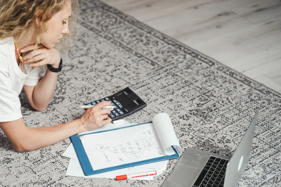 Indépendante qui calcule son tarif journalier avec une calculatrice, des notes et un ordinateur